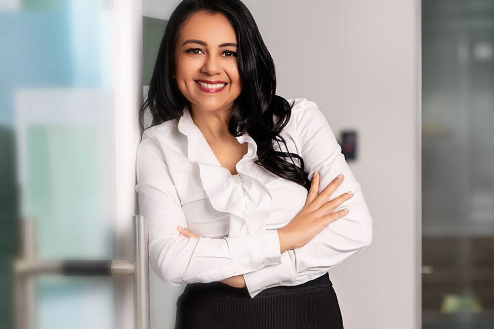 Smiling professional woman in white blouse standing confidently in office environment.