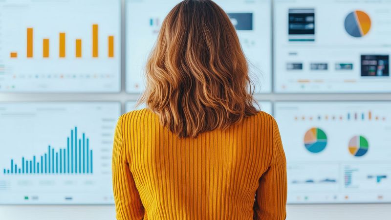 Woman analyzing data on multiple digital screens with colorful graphs and charts.
