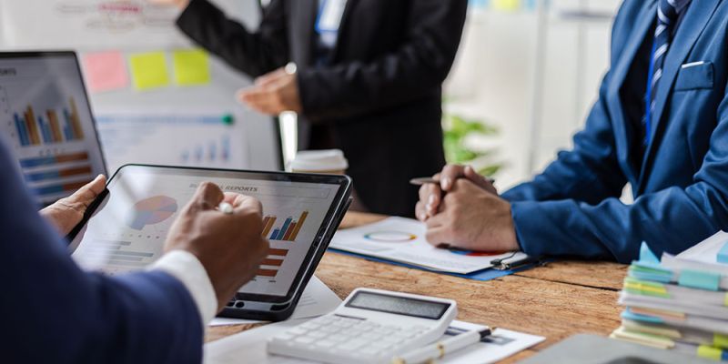 Business team analyzing charts on tablet and documents during a meeting, with a whiteboard in the background.