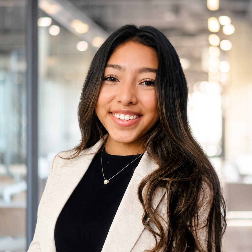 Smiling woman in professional attire stands in a modern office environment.