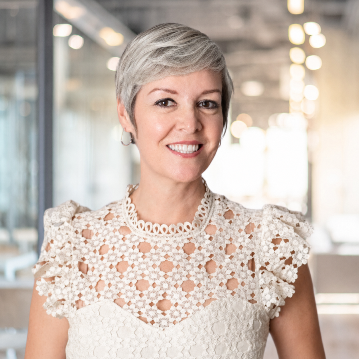 Woman in a lace top smiling in a modern office setting.